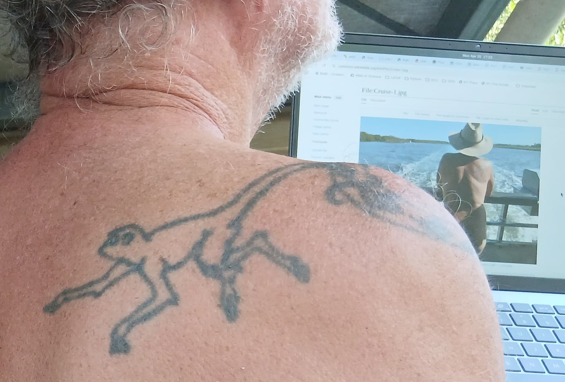 Man with tattoo in front of a laptop showing Wikimedia Commons