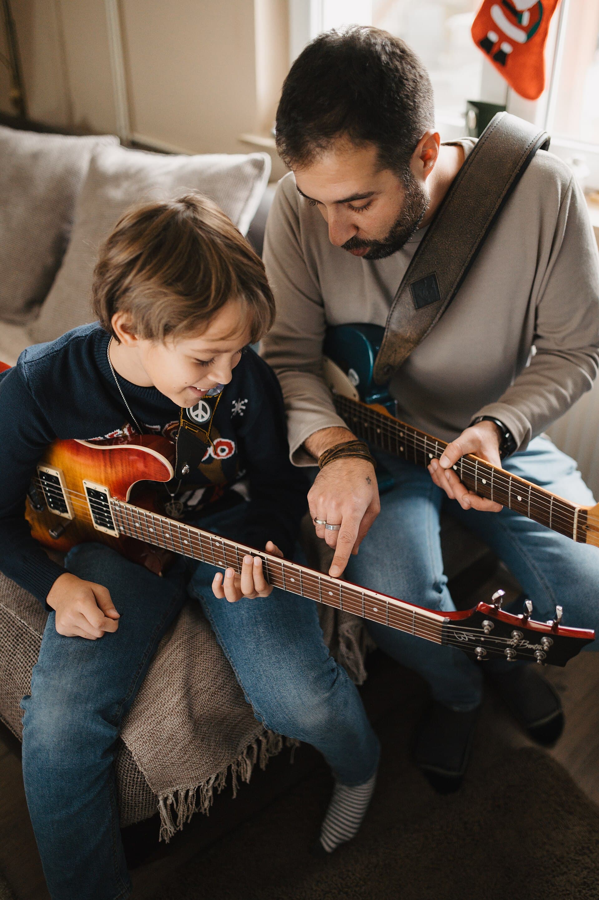 A father is showing his son how to play the guitar in a cozy living room setting