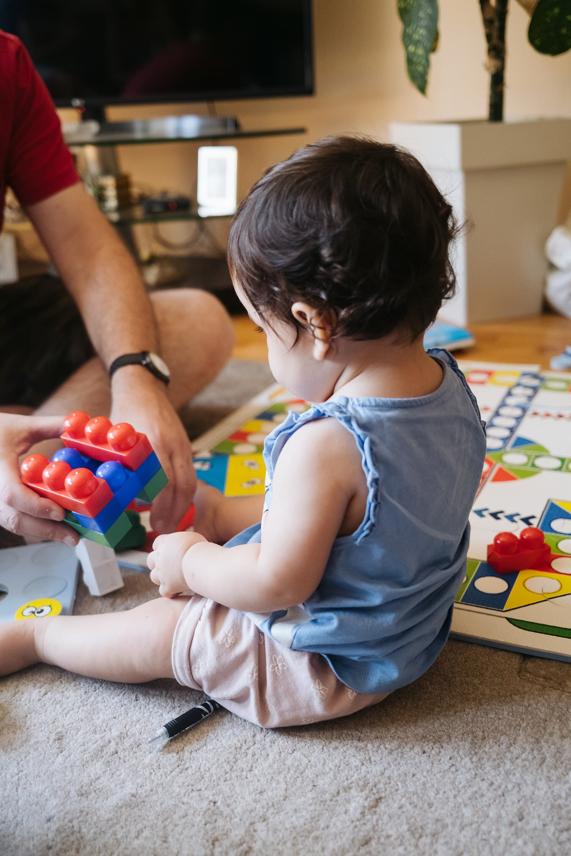 Child playing with colorful building blocks on the floor with adult in a cozy living room