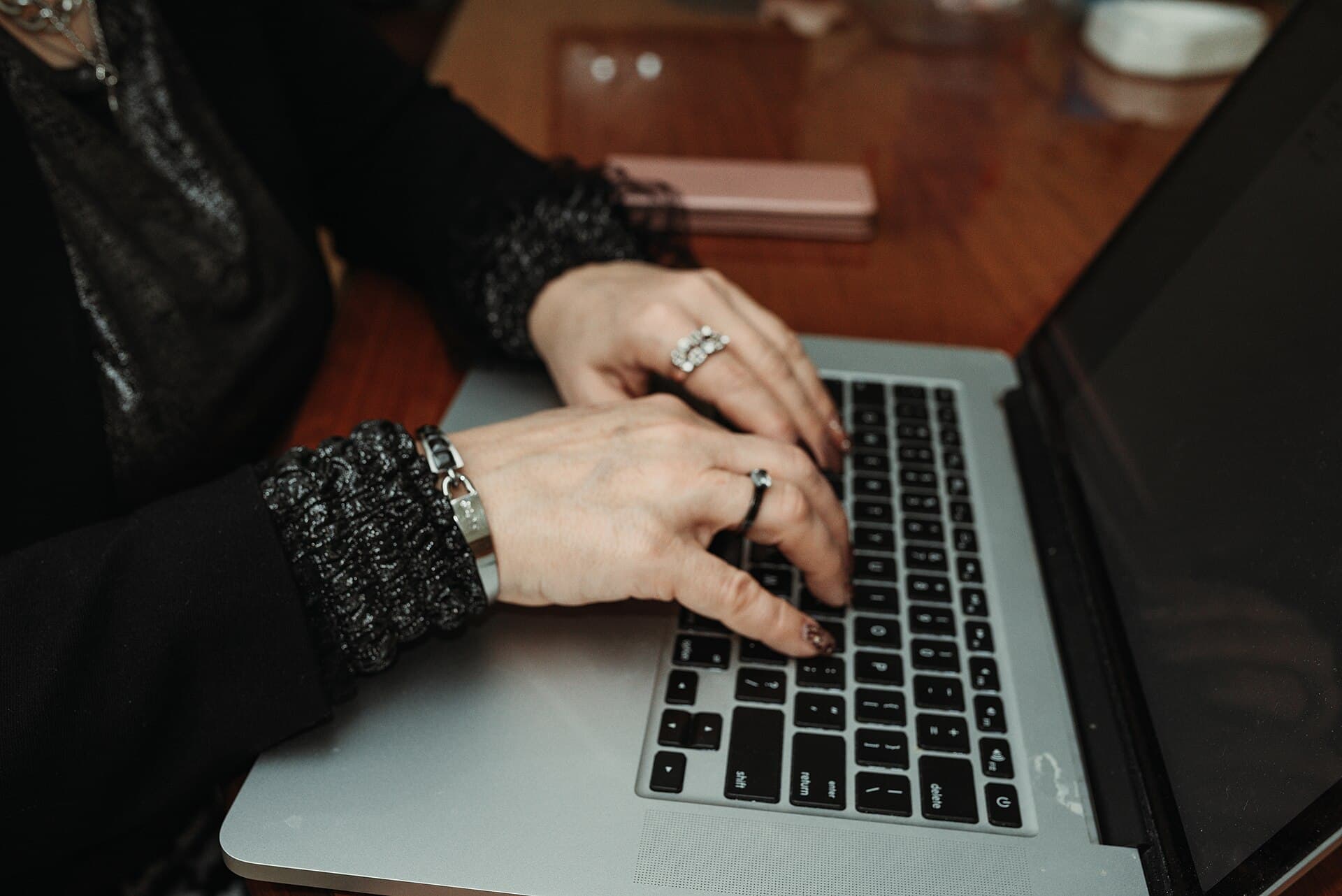 Hands typing on a laptop at a wooden table during a casual indoor setting with a relaxed atmosphere