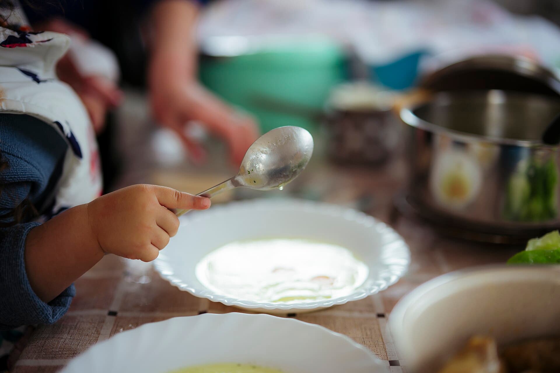 Child's hand holding a spoon over a plate while preparing food in a kitchen